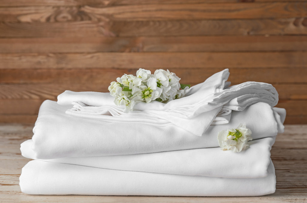 Folded white Pizuna bedding set styled with floral accents for a fresh, minimalist look